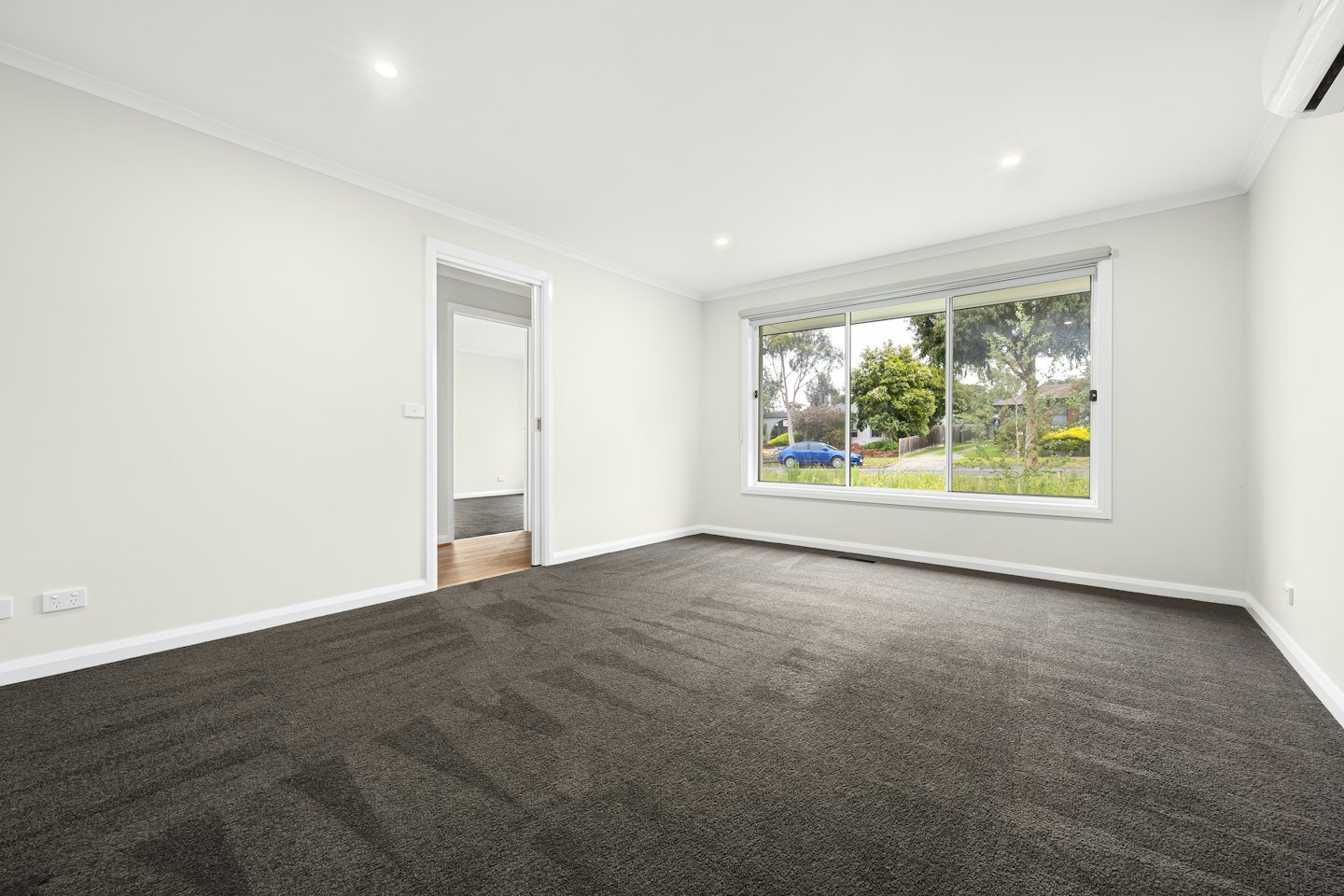 Empty room with grey carpet and a view of suburban trees.